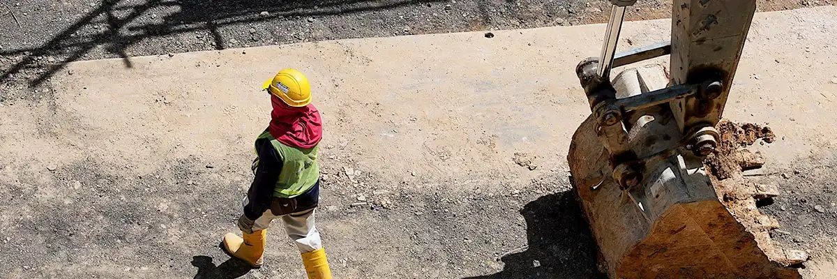 Contruction worker walking past back hoe